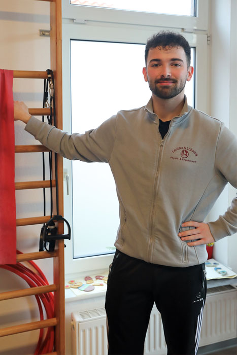 An einer Sprossenwand steht ein junger Mann.