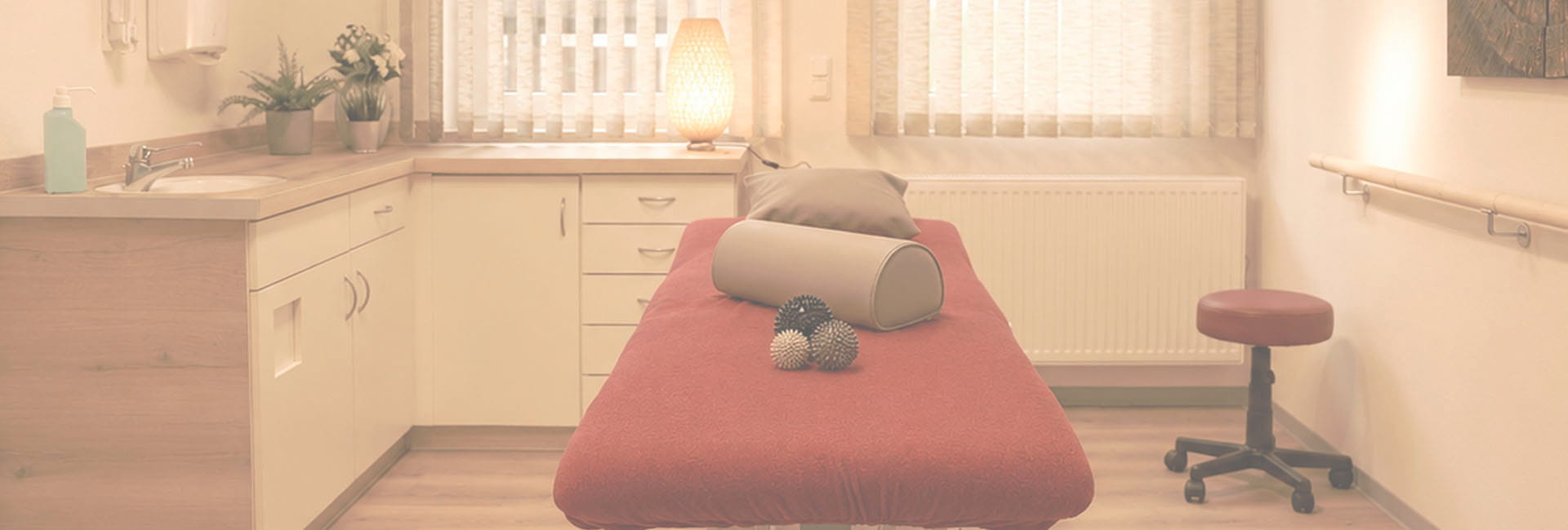 Behandlungsraum mit roter Therapieliege, Waschbecken, Handlauf und Hocker